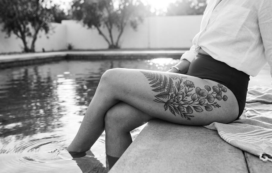 Person with a botanical thigh tattoo sitting beside a swimming pool