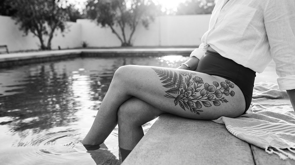 Person with a botanical thigh tattoo sitting beside a swimming pool