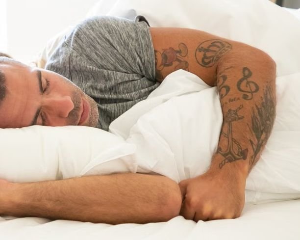 Man with arm tattoos sleeping peacefully in bed