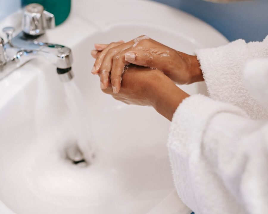 Hands lathering fragrance-free liquid soap under running water at a bathroom sink