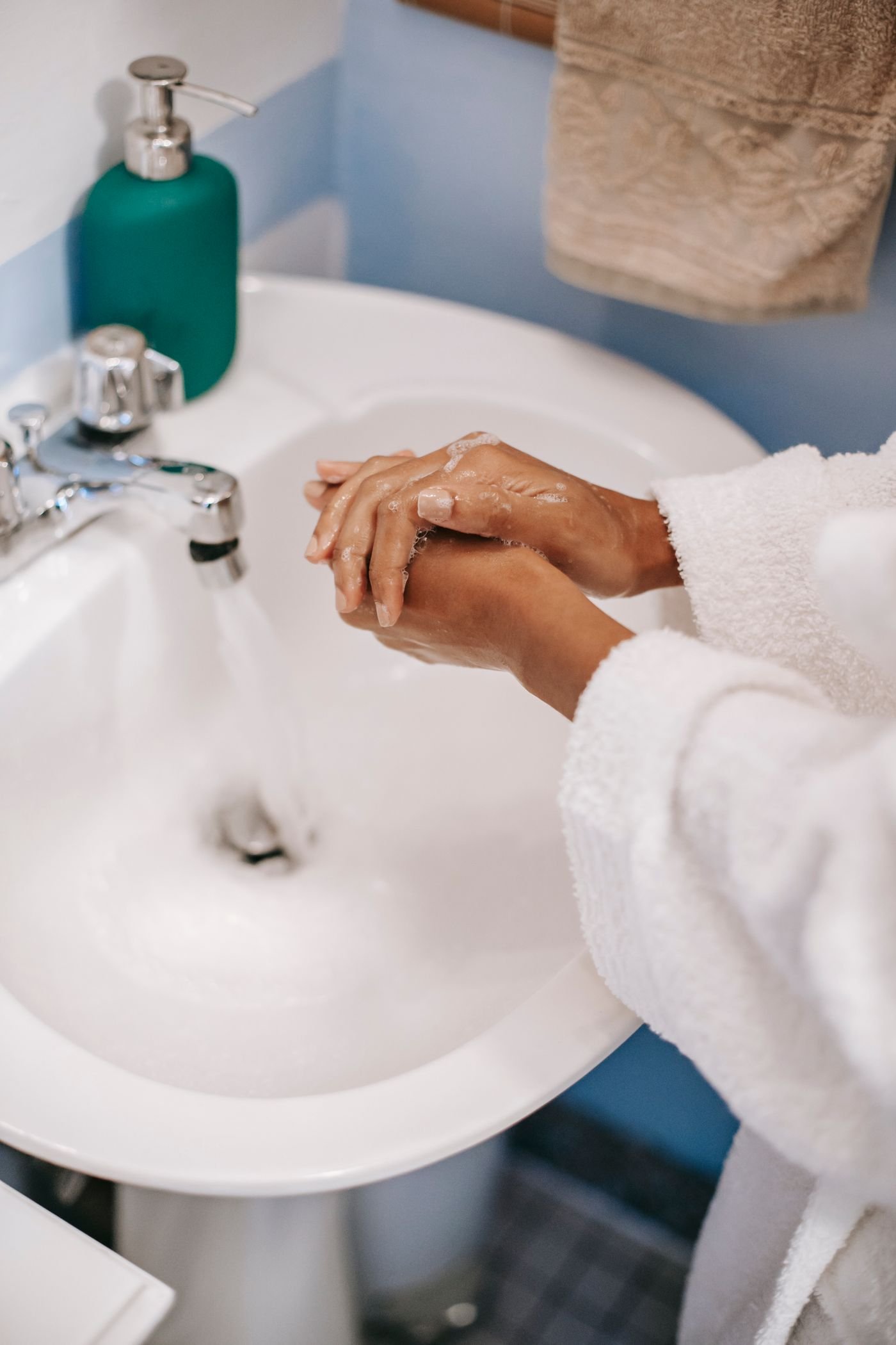 Hands lathering fragrance-free liquid soap under running water at a bathroom sink