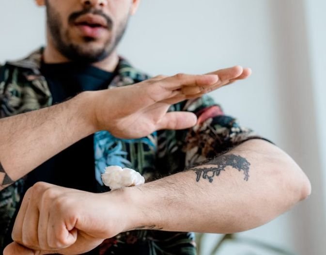 Man with a forearm tattoo applying moisturizing cream to healing skin