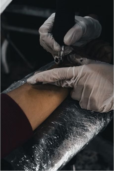 Tattoo artist working on a fresh tattoo with second skin plastic film wrapped around the arm