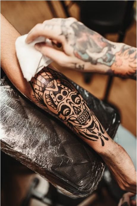 Tattoo artist wiping down a fresh skull tattoo wrapped in second skin film
