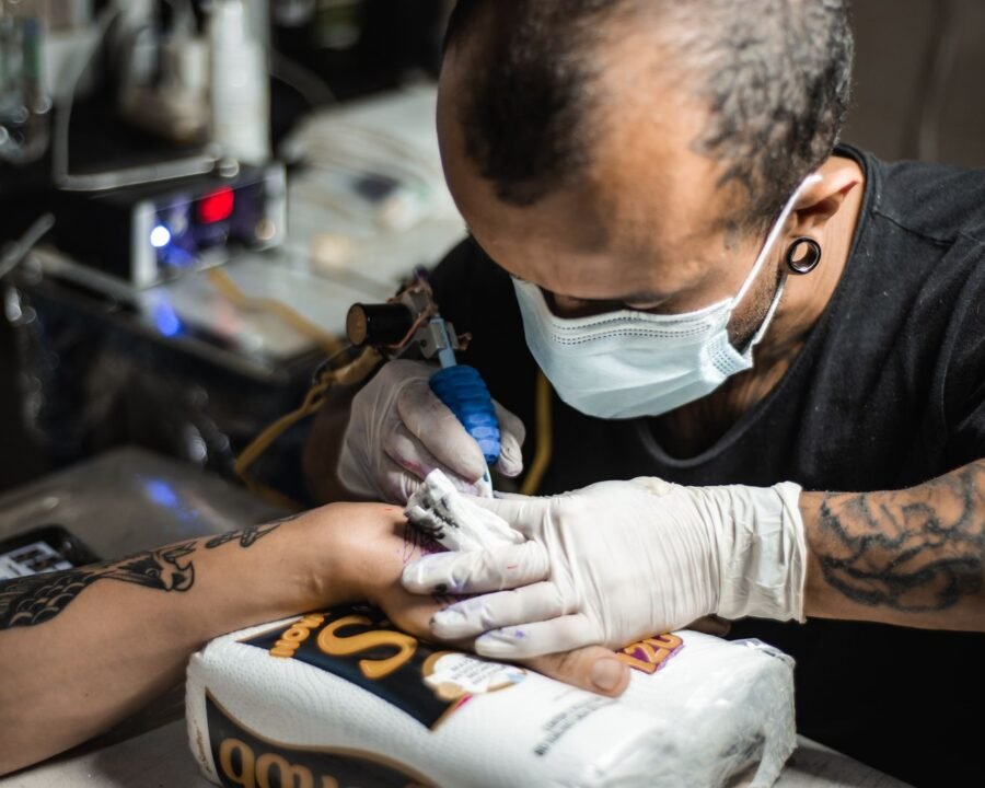 Gloved tattoo artist working on a hand tattoo, a high-pain spot where clients ask about tattoo numbing cream