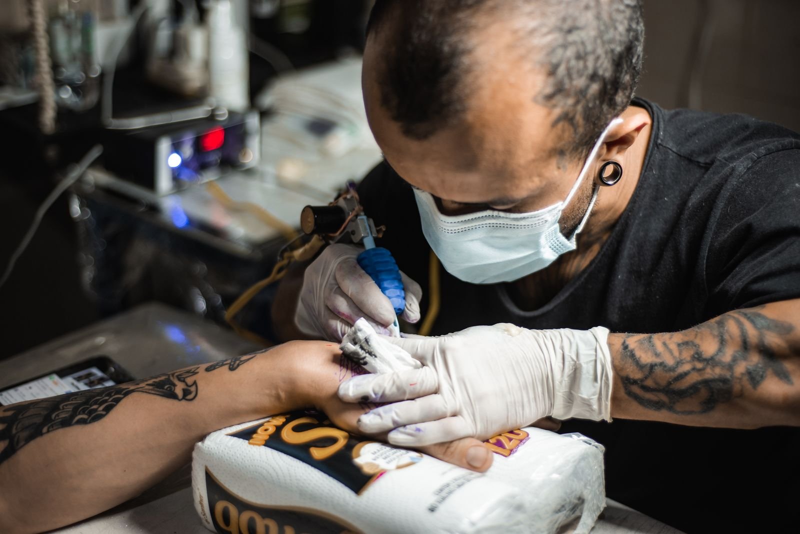 Gloved tattoo artist working on a hand tattoo, a high-pain spot where clients ask about tattoo numbing cream