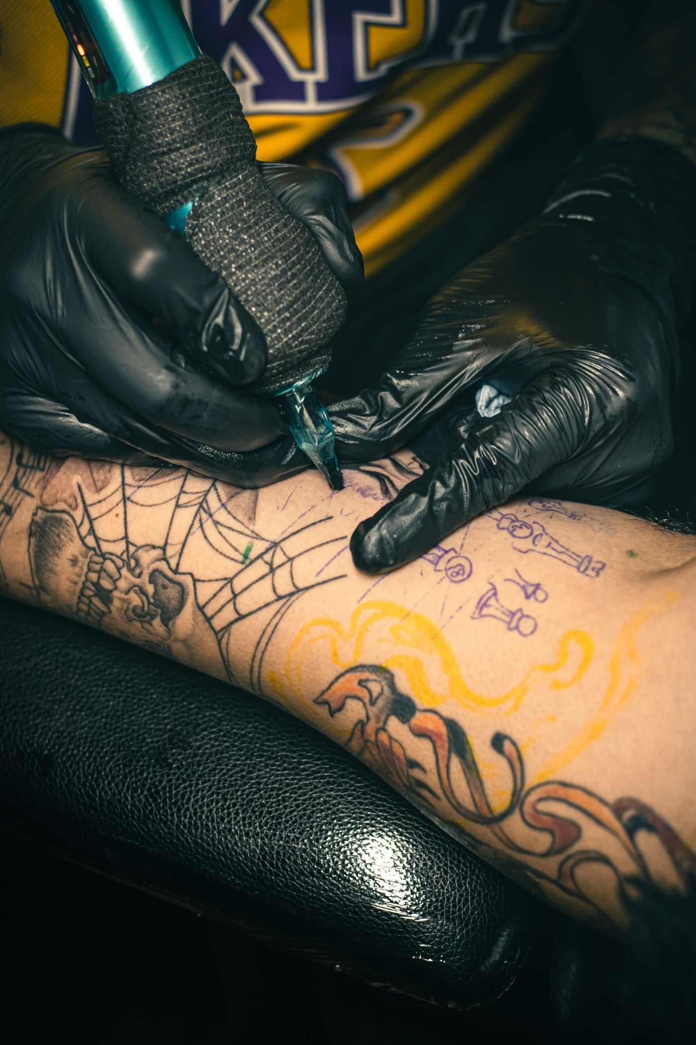 Close-up of a tattoo machine working on a heavily tattooed forearm during a session