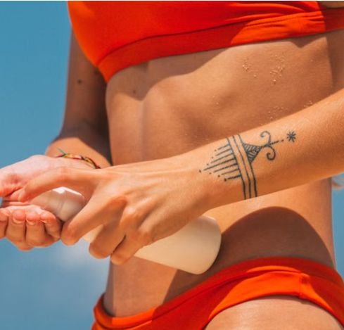 Person with a wrist tattoo applying sunscreen at the beach